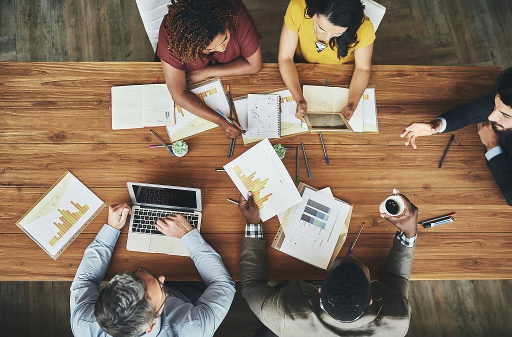 overhead shot of diverse group of people sitting at at a table, reviewing reports.