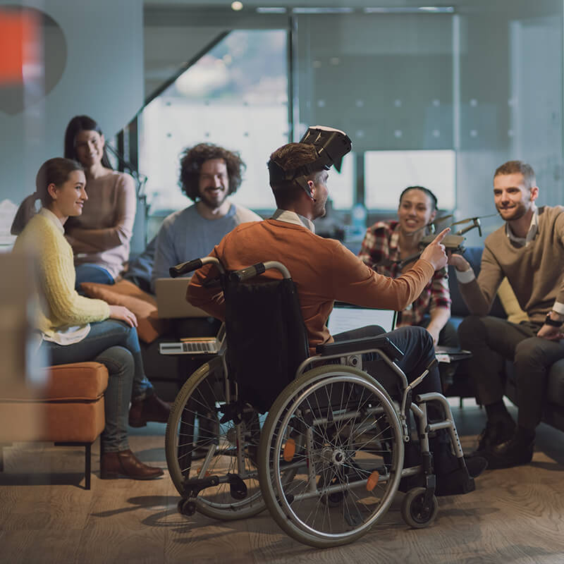 A group of people demonstrating drone technology, man in the foreground is in a wheelchair with a VR headset.